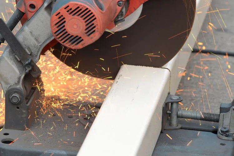 Chop saw with an abrasive cutting disc cutting square steel tube in a metal fabrication workshop